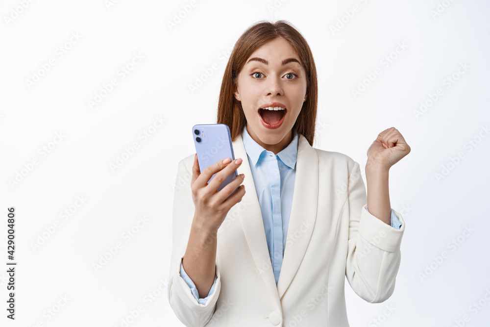She is winner. Lucky corporate woman scream from joy, winning on mobile phone, triumphing from good news in internet, holding cellphone and jumping from happiness, white background She is winner. Lucky corporate woman scream from joy, winning on mobile phone, triumphing from good news in internet, holding cellphone and jumping from happiness, white background
