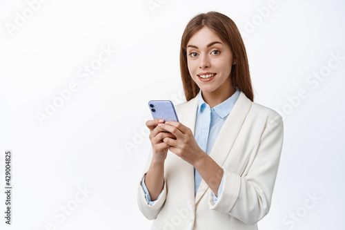 Girl in corporate suit hold smartphone and smiles at camera. Professional office woman using mobile phone, wearing business suit, white background