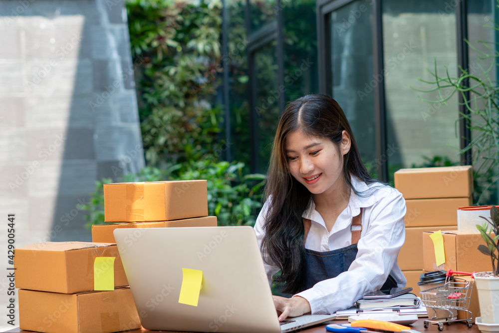 Young smiling beautiful owner asian woman freelance sme business online shopping working on laptop computer with parcel box on desk at home - SME business online and delivery concept Young smiling beautiful owner asian woman freelance sme business online shopping working on laptop computer with parcel box on desk at home - SME business online and delivery concept