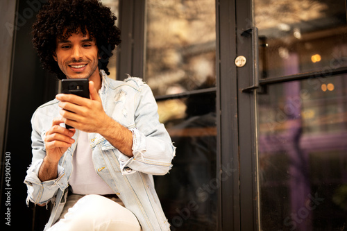 Young man enjoying outdoors. Handsome man with curly hair using the phone