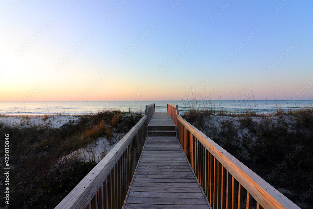 A boardwalk shows the way to the beach over the dunes as a new day's sunrise appears.