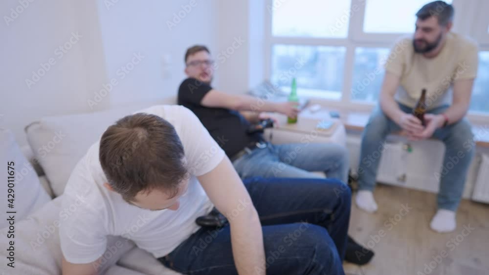 Friends are sitting on the couch and getting ready to play the console with beer. Fun pastime. They do cheers together Friends are sitting on the couch and getting ready to play the console with beer. Fun pastime. They do cheers together