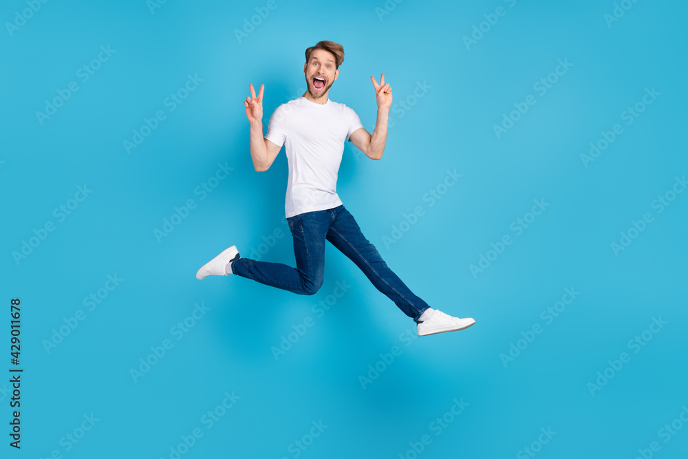 Full size portrait of energetic cheerful man open mouth fingers show v-sign isolated on blue color background