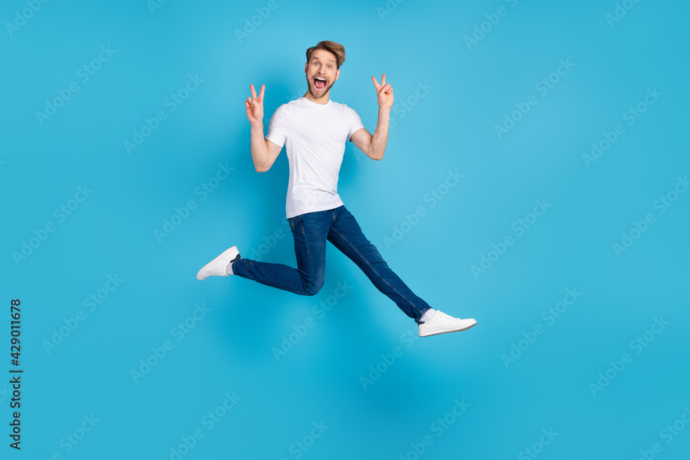 Full size portrait of energetic cheerful man open mouth fingers show v-sign isolated on blue color background Full size portrait of energetic cheerful man open mouth fingers show v-sign isolated on blue color background