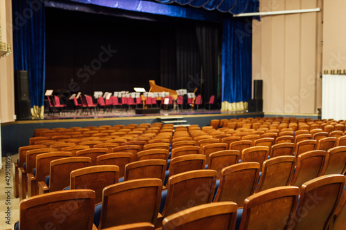 an empty concert hall with free upholstered chairs. musical instruments lie on the stage among the chairs waiting for the orchestra. no audience at the event