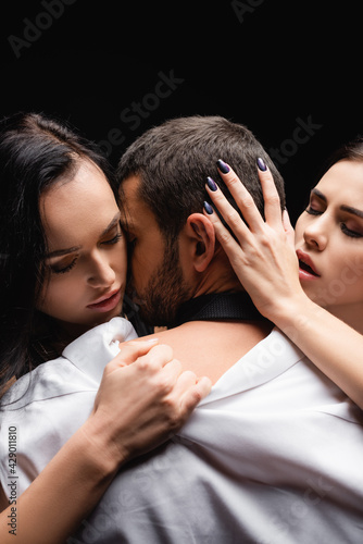 seductive women undressing young businessman isolated on black. © LIGHTFIELD STUDIOS
