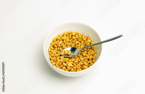 wheat flakes and tablespoon in a white cup on a white background