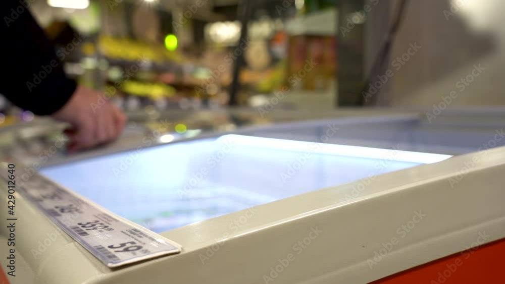 A Shopper with a Cart Comes Up and Opens the Refrigerator in the Store to Retrieve a Pack of Sausages from the Shelf. Buyer Selects Food at Grocery Store Fridge A Shopper with a Cart Comes Up and Opens the Refrigerator in the Store to Retrieve a Pack of Sausages from the Shelf. Buyer Selects Food at Grocery Store Fridge