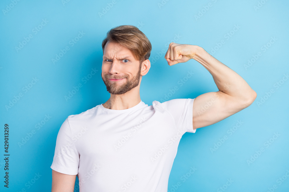 Portrait of focused young man hand flex show biceps look camera isolated on blue color background Portrait of focused young man hand flex show biceps look camera isolated on blue color background