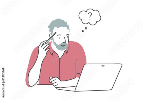 Gray-haired bearded man holding a pen to his temple and looking at laptop.