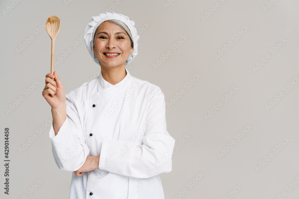 Asian mature woman in chef uniform smiling and holding wooden spoon Asian mature woman in chef uniform smiling and holding wooden spoon
