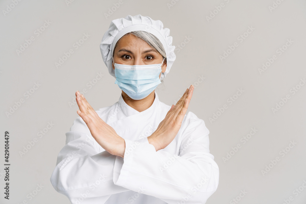 Asian mature woman in chef uniform and face mask gesturing stop sign Asian mature woman in chef uniform and face mask gesturing stop sign