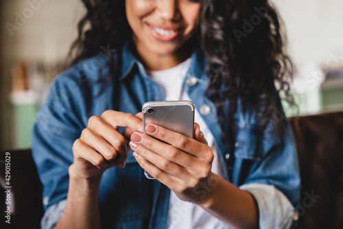Cropped shot of an african-american young woman using smart phone at home. Smiling african american woman using smartphone at home, messaging or browsing social networks while relaxing on couch photo