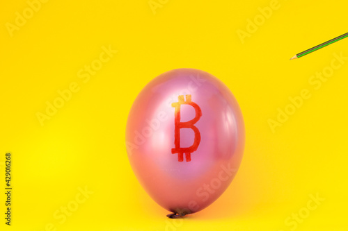 Bitcoin is depicted on a pink balloon on a yellow background with a sharp object that pierces the ball. The concept of rapid decline of cryptocurrency.