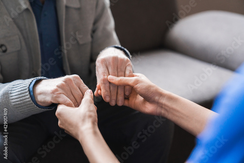 Woman nurse hold hand of elderly grey-haired man showing care and bond close up, female doctor in white coat talk with aged patient, caregiving and nursing service
