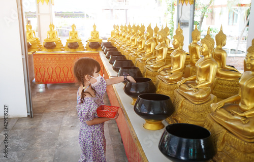 Asian little girl put mask and make merit at the temple. Buddhist make merit, Pay coins photo