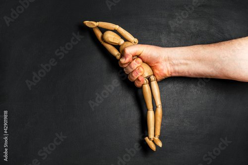 wooden man is grabbed by a man hand. The concept of helplessness and submission