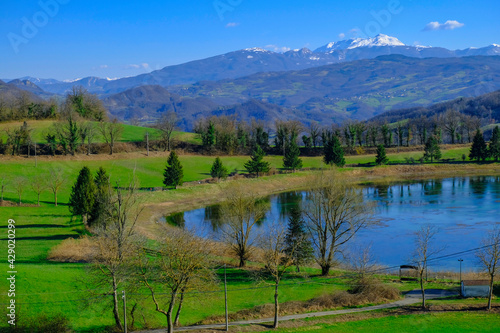Beautiful spring landscape with mountain lake and mountains covered with snow across blue sky. Fir trees, and trees reflected in water.   © Kate