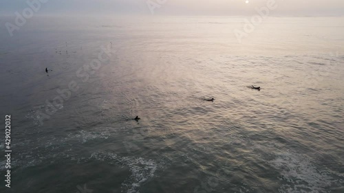 Aerial view of people doing surf in Atlantic Ocean open water at sunset along Caparica coastline, Lisbon, Portugal.
