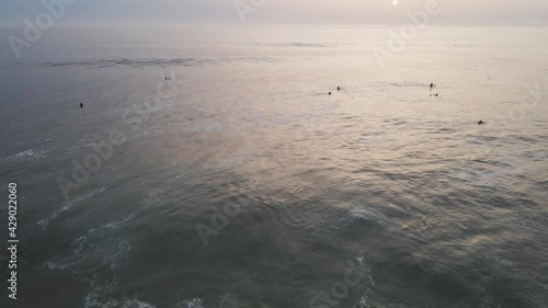 Aerial view of people doing surf in Atlantic Ocean open water at sunset along Caparica coastline, Lisbon, Portugal.
