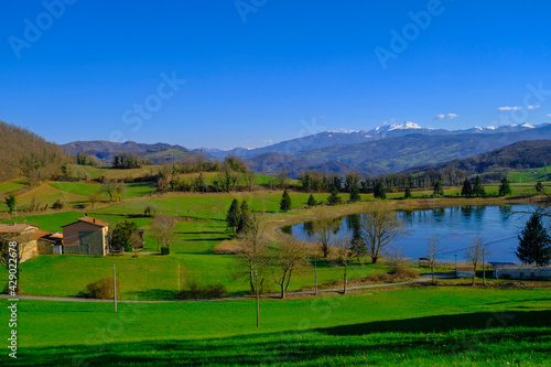 Beautiful spring landscape with mountain lake and mountains covered with snow across blue sky. Fir trees, and trees reflected in water. 