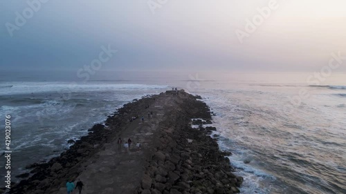 Aerial view of a giant breakwater on the beach in Costa da Caparica facing the Atlantic Ocean with big waves rolling on the beach at sunset, Lisbon, Portugal.