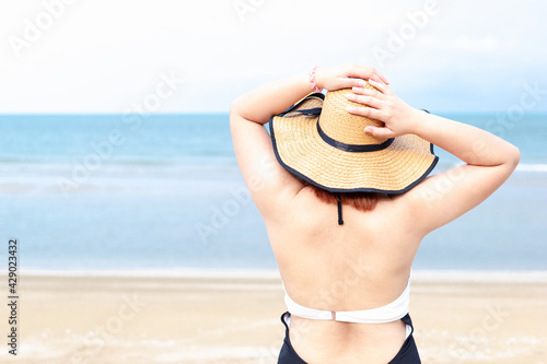 A woman standing with her back in a swimming dress and a sun hat on the beach.Beach vacation.Copy space. photo