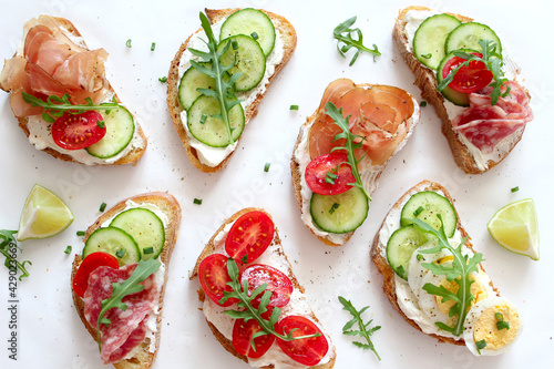 Variety of sandwiches with light cheese, vegetables and salami on light background. Top view.