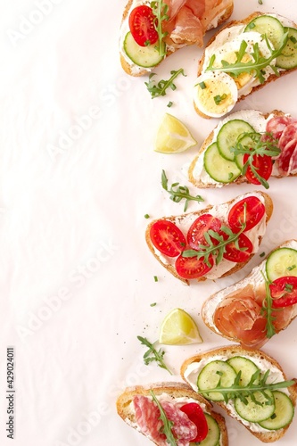 Variety of sandwiches with light cheese, vegetables and salami on light background. Top view.