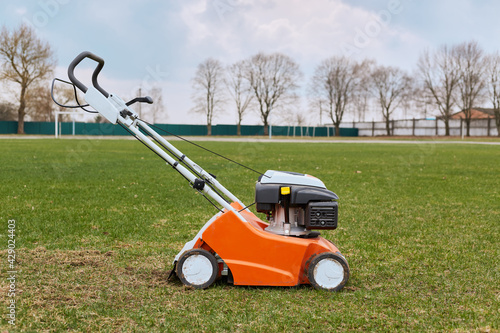 Mowing or cutting long grass with lawn mower. Gardening, taking care of sward. Side view of special equipment in field on background of grass, trees and sky,