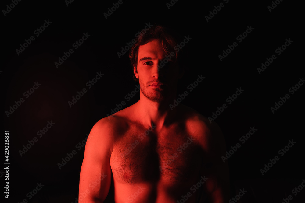 Fototapeta premium red lighting on sexy shirtless man looking at camera isolated on black.