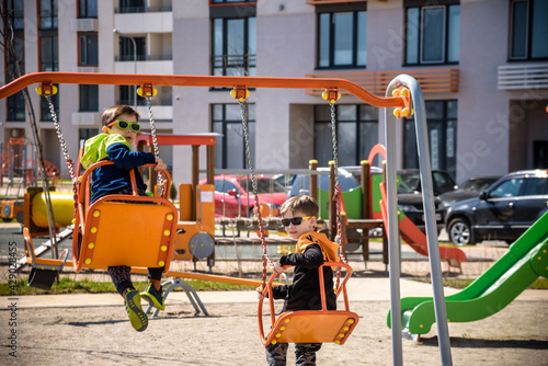 Two European boys swing on a swing in the summer holidays. Children have fun outdoors