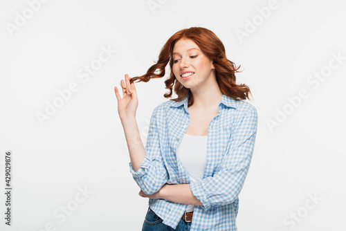 positive young woman in blue checkered shirt adjusting hair isolated on white.