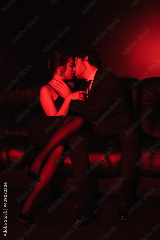 red lighting on sexy couple kissing on black leather sofa. red lighting on sexy couple kissing on black leather sofa.