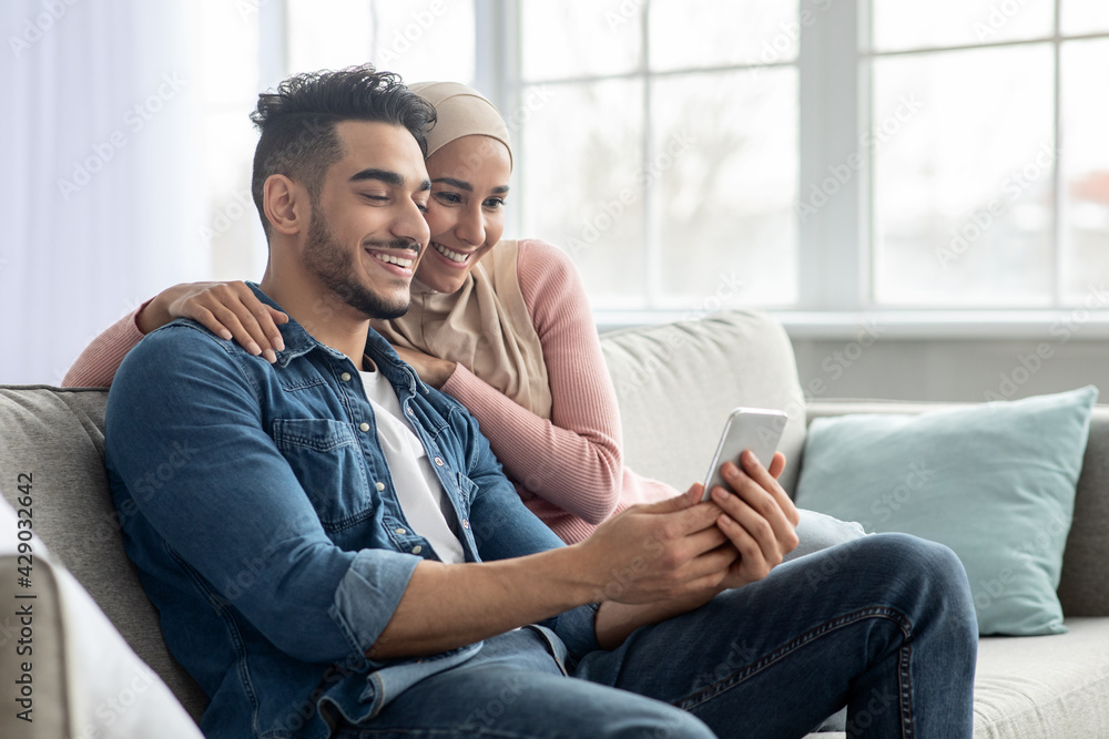 © Prostock-studio - Happy middle-eastern couple using mobile phone at home © Prostock-studio - Happy middle-eastern couple using mobile phone at home