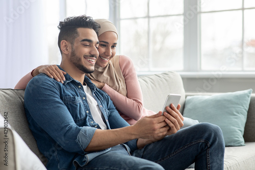 Happy middle-eastern couple using mobile phone at home