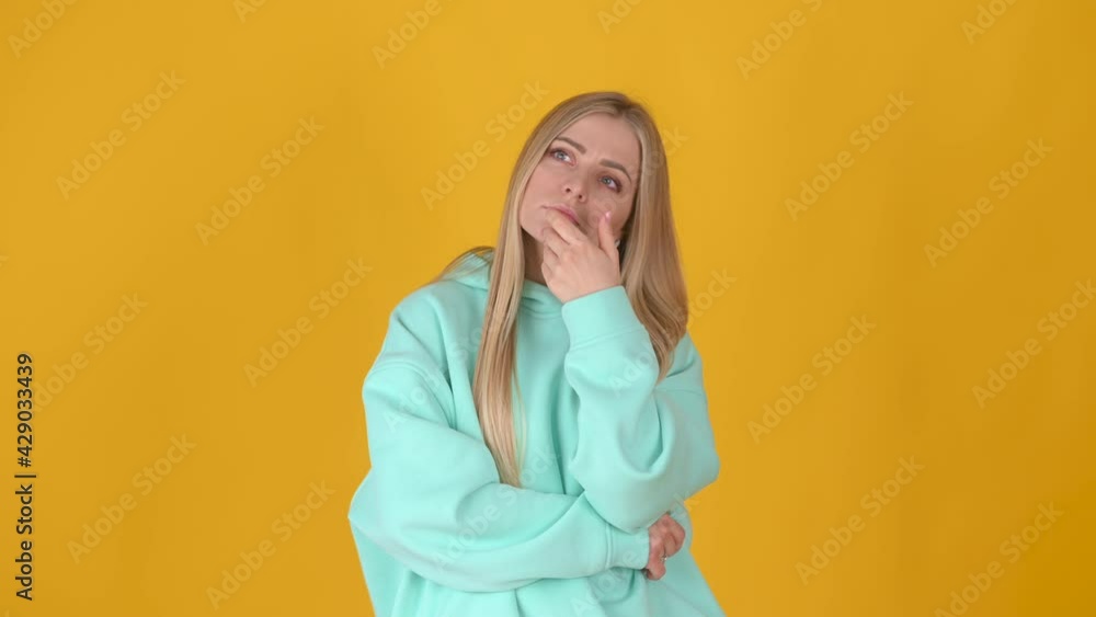 Young blond woman is thinking about something standing isolated on yellow studio background. pondering and musing answer. Young blond woman is thinking about something standing isolated on yellow studio background. pondering and musing answer.