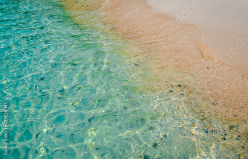High angle of The sandy beach and the crystal clear blue water sparkling.