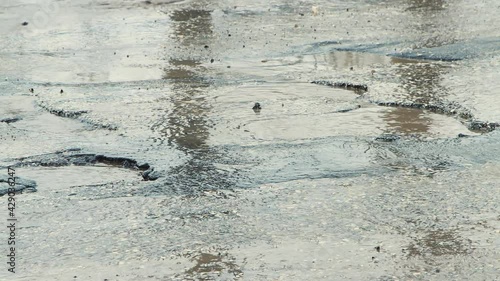 Fast driving of car wheels on a bad road with muddy puddles, holes and cracks. A crumbling road with potholes. Old asphalt pavement made in violation of technology. Taxpayer money is wasted.