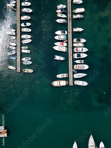 Aerial top down view of boat dock and yacht port in Budva, Montenegro. White private motor boats are moored to pier on Adriatic sea coast. Yacht club boats parking. Photo from drone. Minimalism.