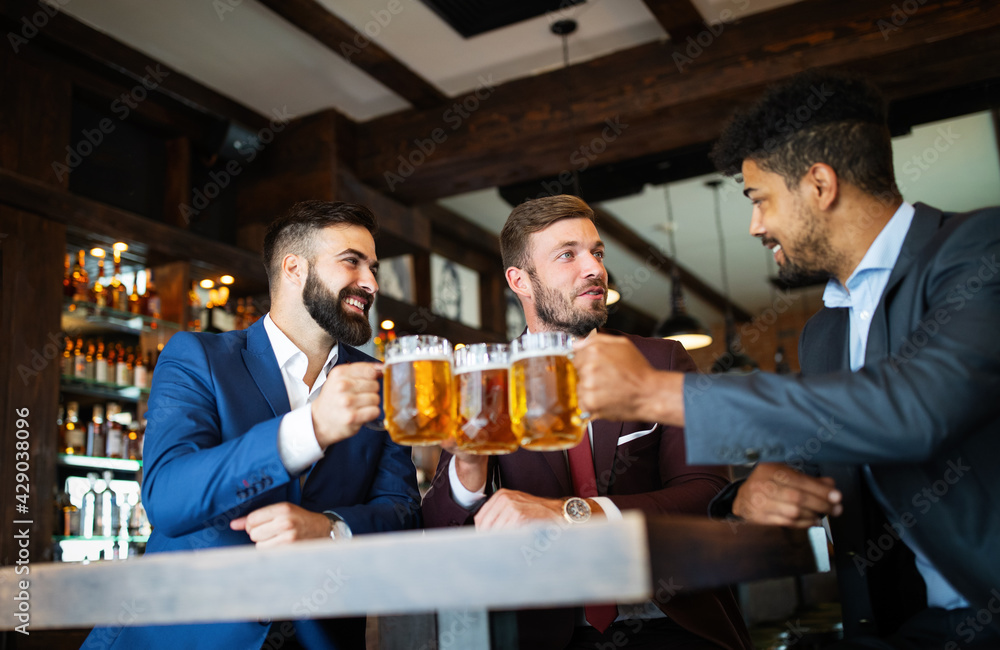 Happy young businessmen drinking beer and talking at pub after work