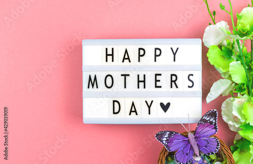 Happy Mother's Day text background, text message on a lightbox, pink workspace with spring flowers, holiday concept