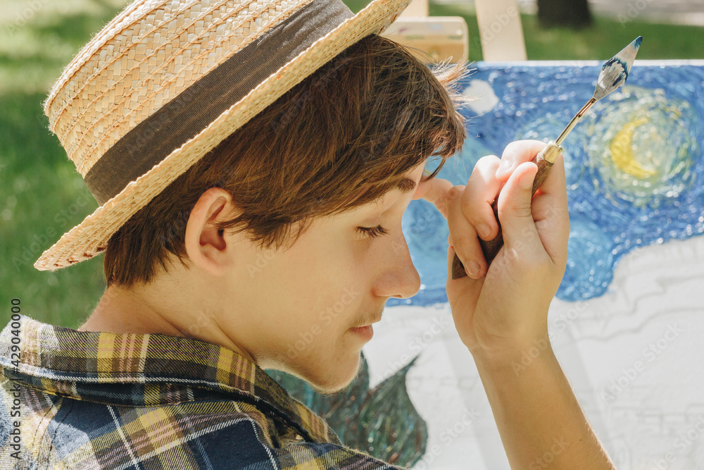 Φωτογραφία a young guy in a straw hat sits in the park in front of an easel and paints a picture with oil paints