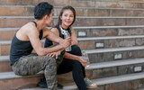 Asian adult sportive and healthy couple wearing black shirts, headphone, talking, smiling with happiness and sitting on steps after doing exercise.