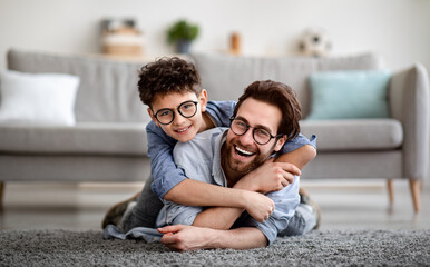 Parents and children being friends. Joyful father and son having fun, dad lying on floor, carrying boy on back