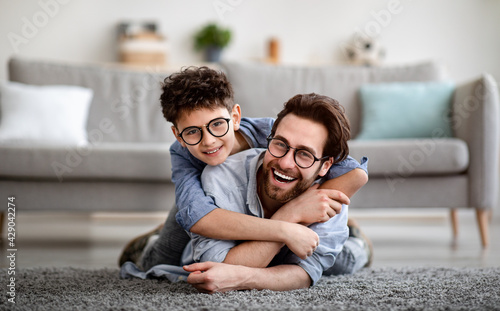 Parents and children being friends. Joyful father and son having fun, dad lying on floor, carrying boy on back