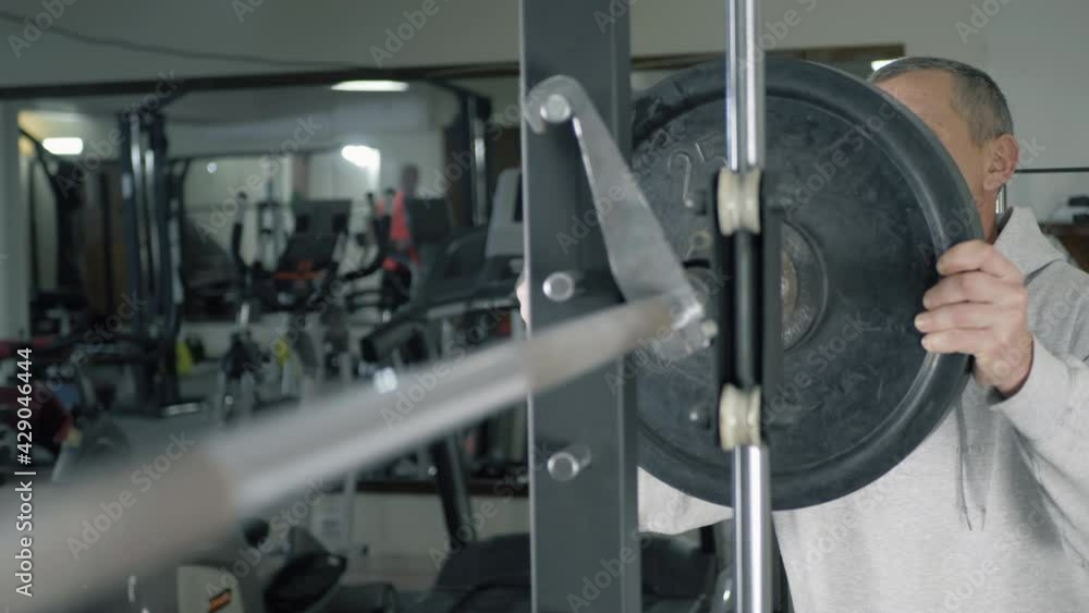 Bodybuilder puts weight plate on barbell in the gym. Athlete increases weight of the barbell during training. Focus in the foreground Bodybuilder puts weight plate on barbell in the gym. Athlete increases weight of the barbell during training. Focus in the foreground