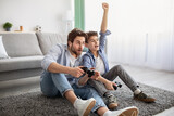 Father-son competition. Joyful boy winning dad in videogame and raising hand, celebrating victory