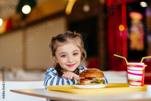 Little girl eats burger in cafe