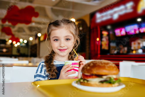 Little cute girl eating a sandwich in a cafe  concept of a children s fast food meal